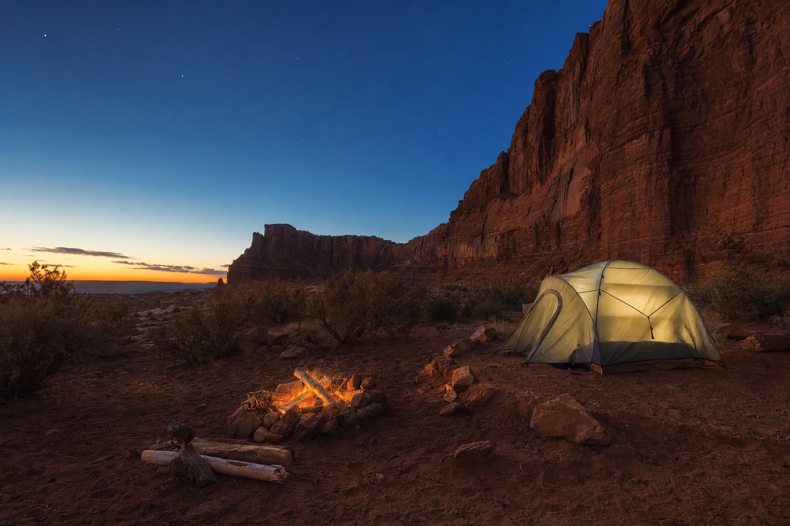 A quiet desert campsite near red sandstone cliffs at dusk