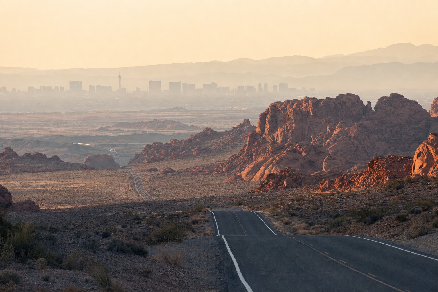 A desert highway leading from a distant city skyline toward red sandstone mountains