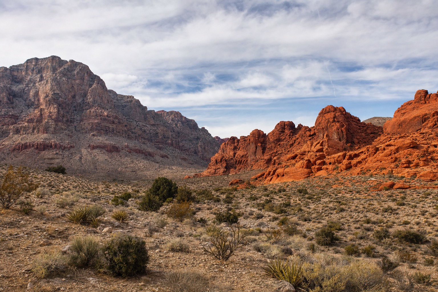 A panoramic desert vista blending red sandstone cliffs on one side with brighter red-orange rock formations on the other