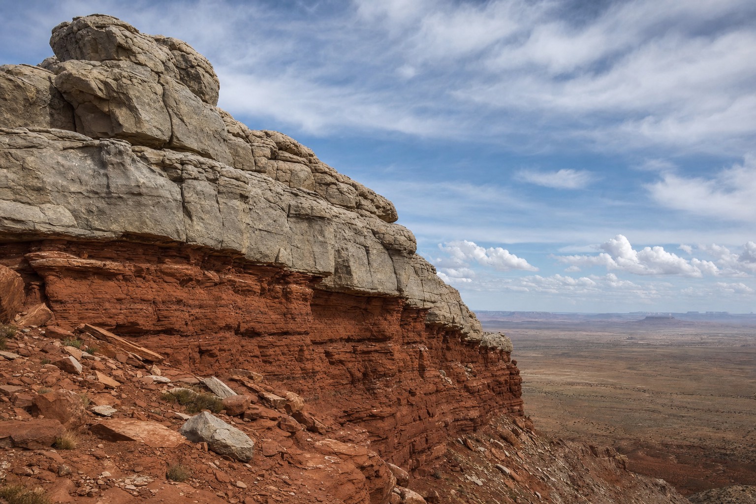 A dramatic desert escarpment where grey limestone caprock sits above red sandstone cliffs